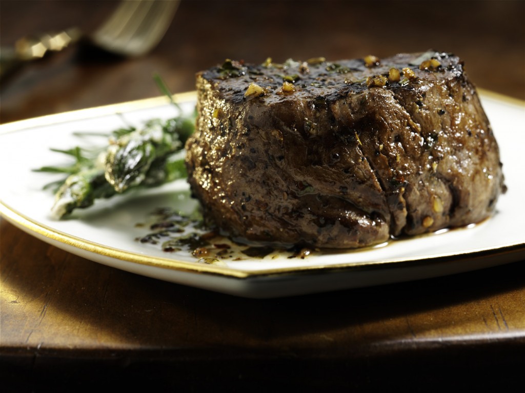 A close-up of a beef filet plate, presented in detail on a square white plate that's lined with gold on the outside edge.